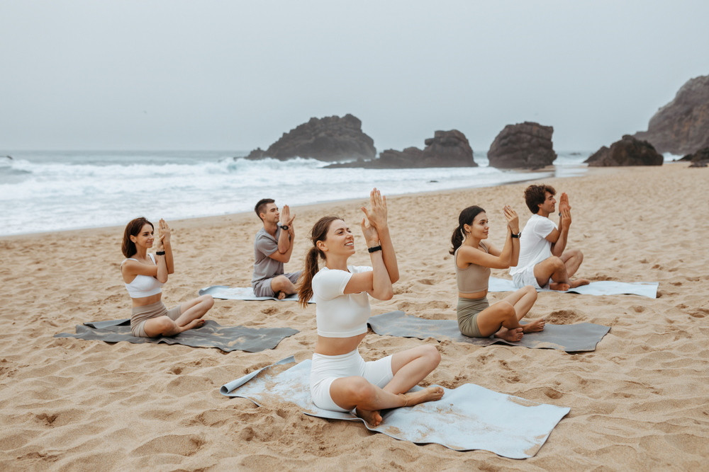 Gruppo di uomini e donne che pratica yoga sulla spiaggia